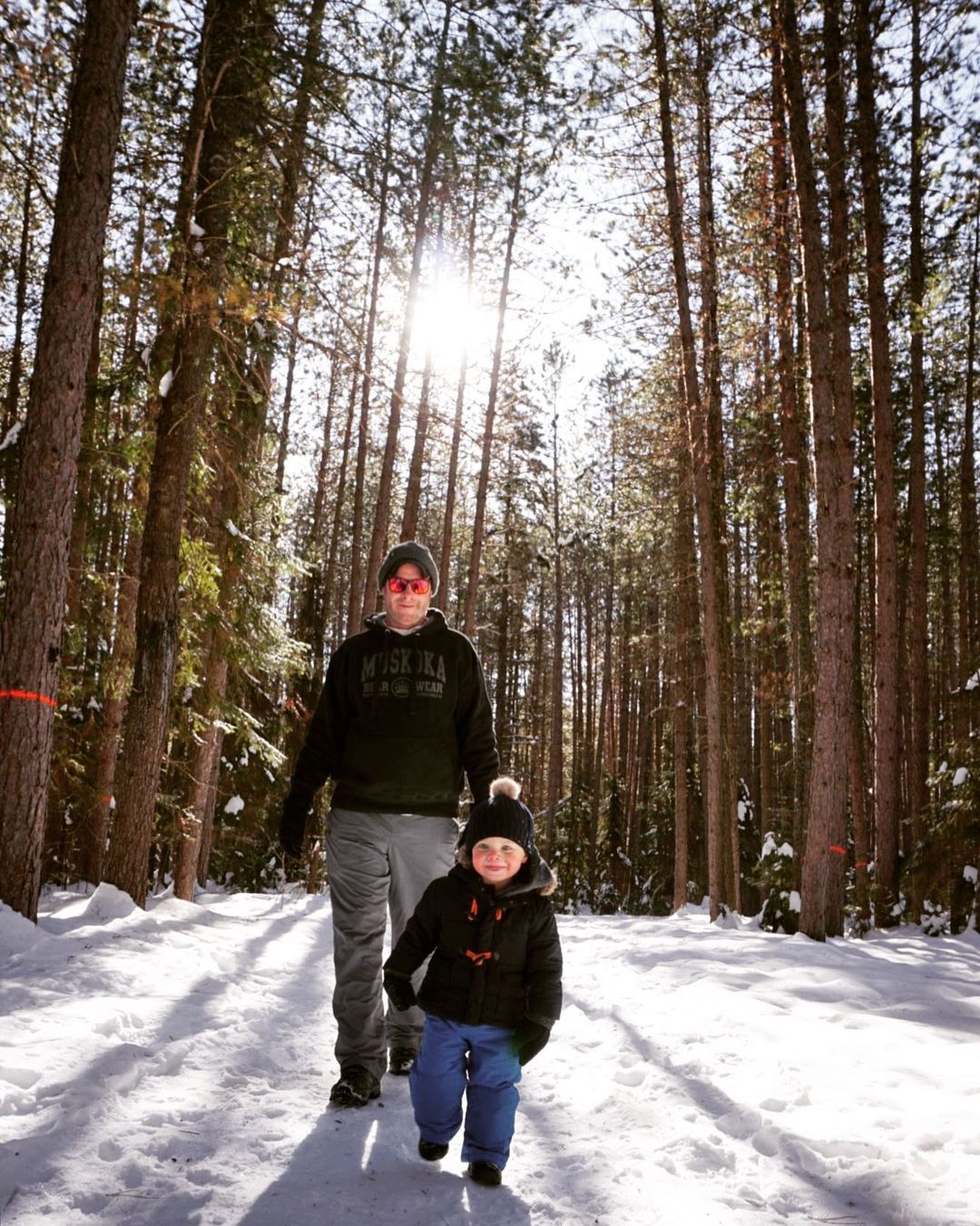 Photo of a dad and son walking in the winter forest. Dad is wearing a black muskoka bear wear hoodie