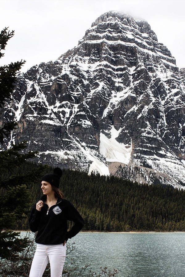 Canadian Woman standing in front of Banff mountains and lake wearing a black MBW quarter-zip sweater and white jeans
