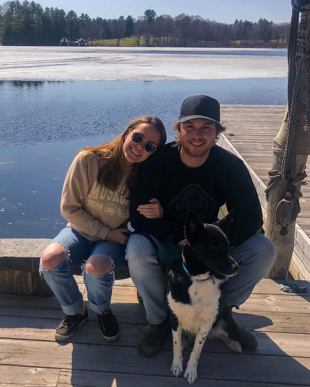 Canadian man and woman sitting on a dock wearing Muskoka Bear Wear posing with their dog