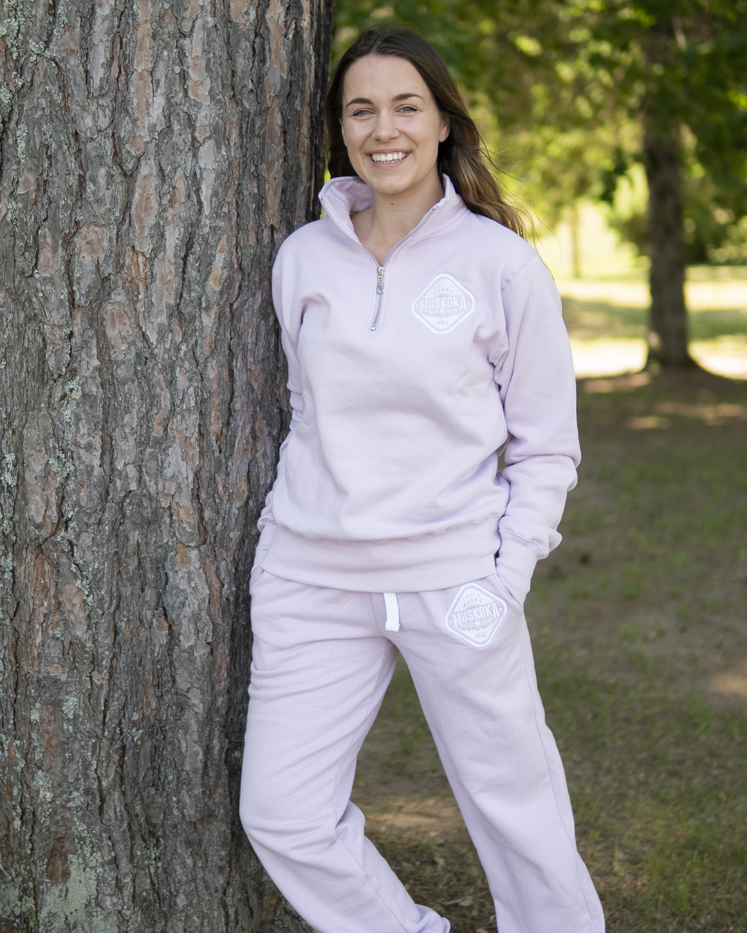Canadian Influencer Kresson wearing a Soft Violet Quarter Zip and matching Soft Violet MBW Camp Pants (sweatpants) is leaning against a tree outside and smiling.