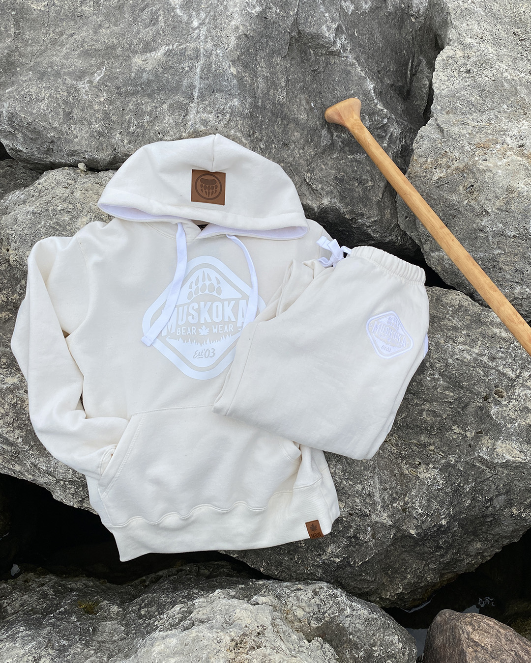 Aerial shot of Ivory Hoody and Ivory sweatpants laying on a rock with a wooden paddle peeking in to photo.
