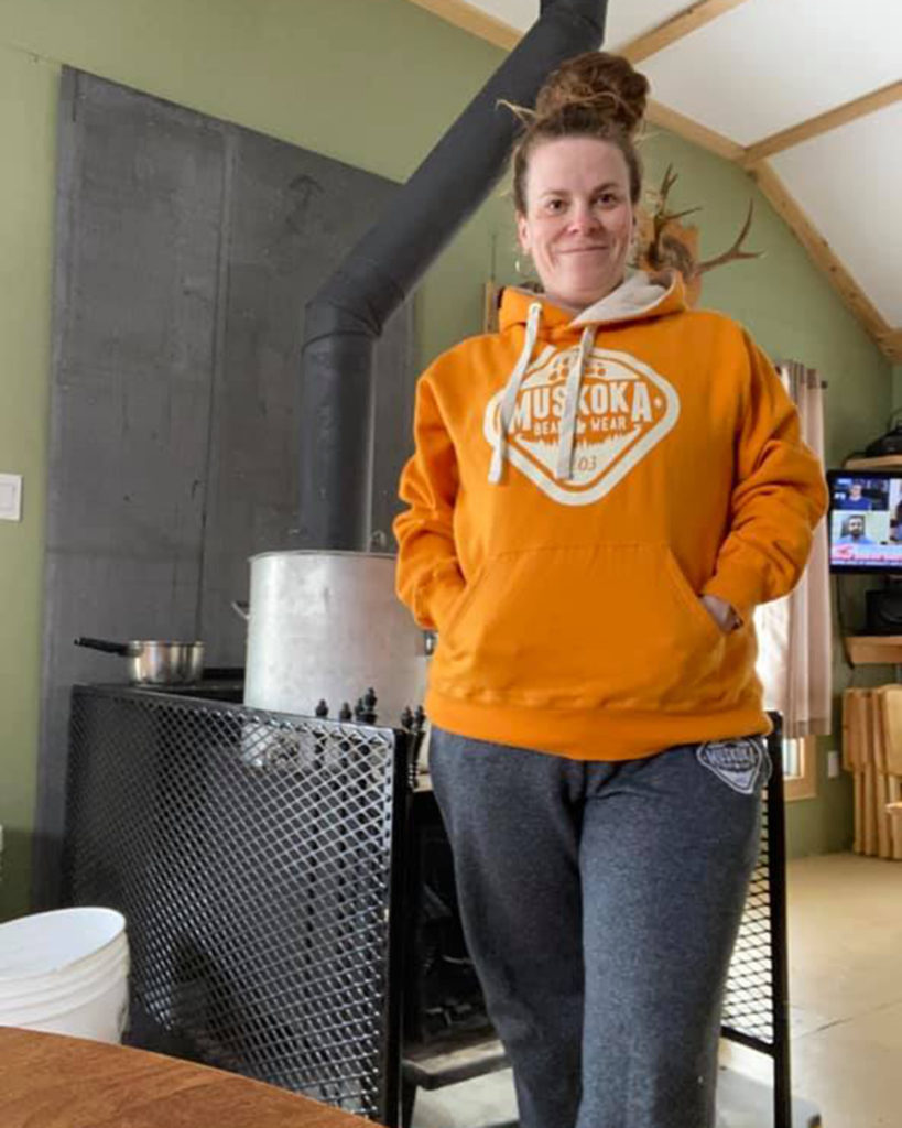 Woman standing in cottage wearing orange MBW hoody and grey MBW sweatpants